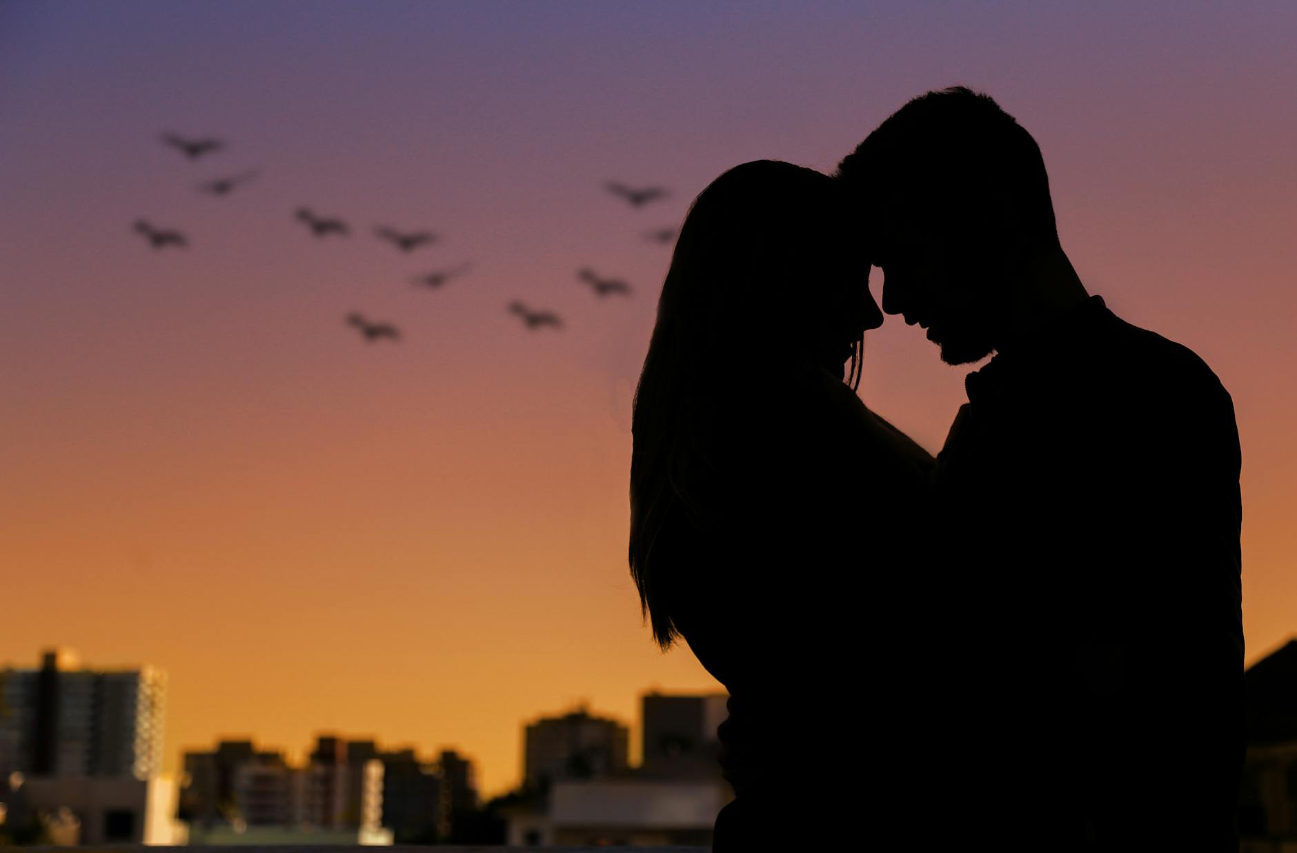 Silhouette of a couple embracing at sunset in an urban setting, evoking romance.